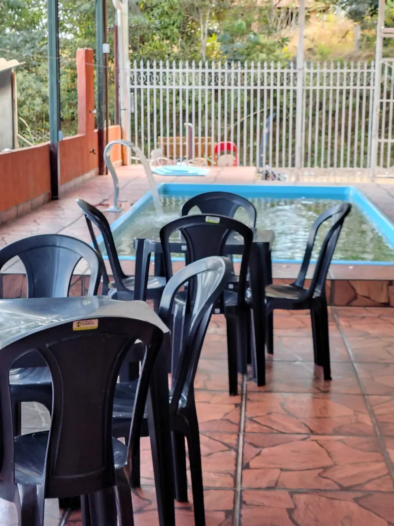 Piscina de borda azul com mesas e cadeiras pretas ao redor, no piso de pedra